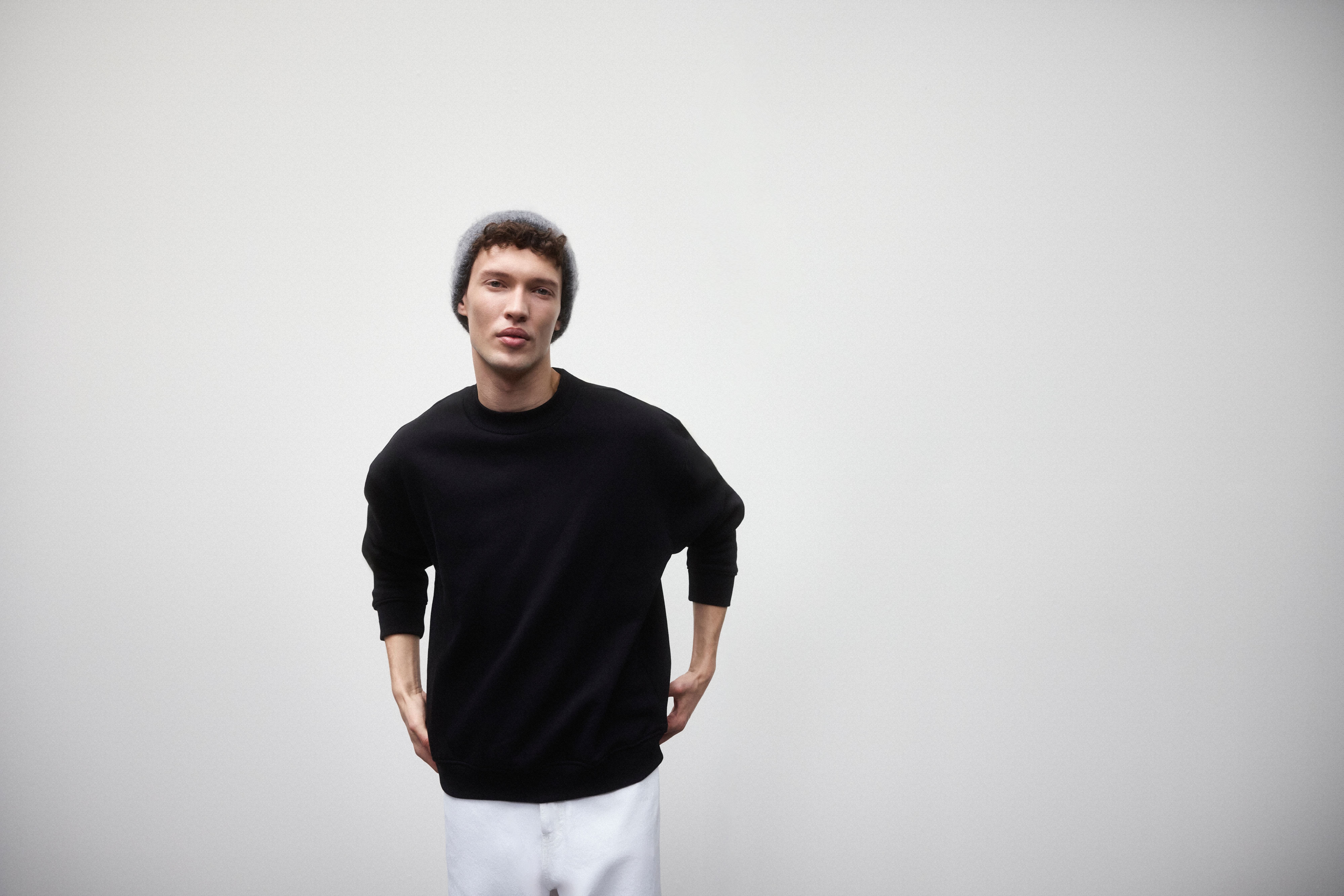 Homme portant un sweatshirt noir, un jean blanc et un bonnet gris